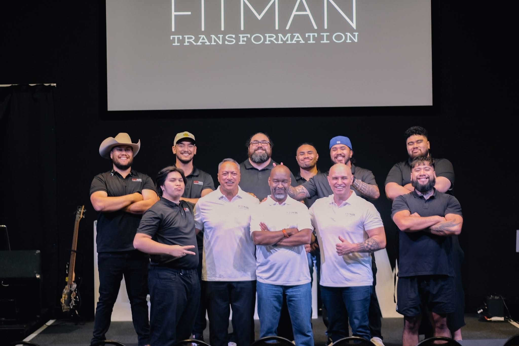 A group of men on stage beneath the FITMAN Transformation screen